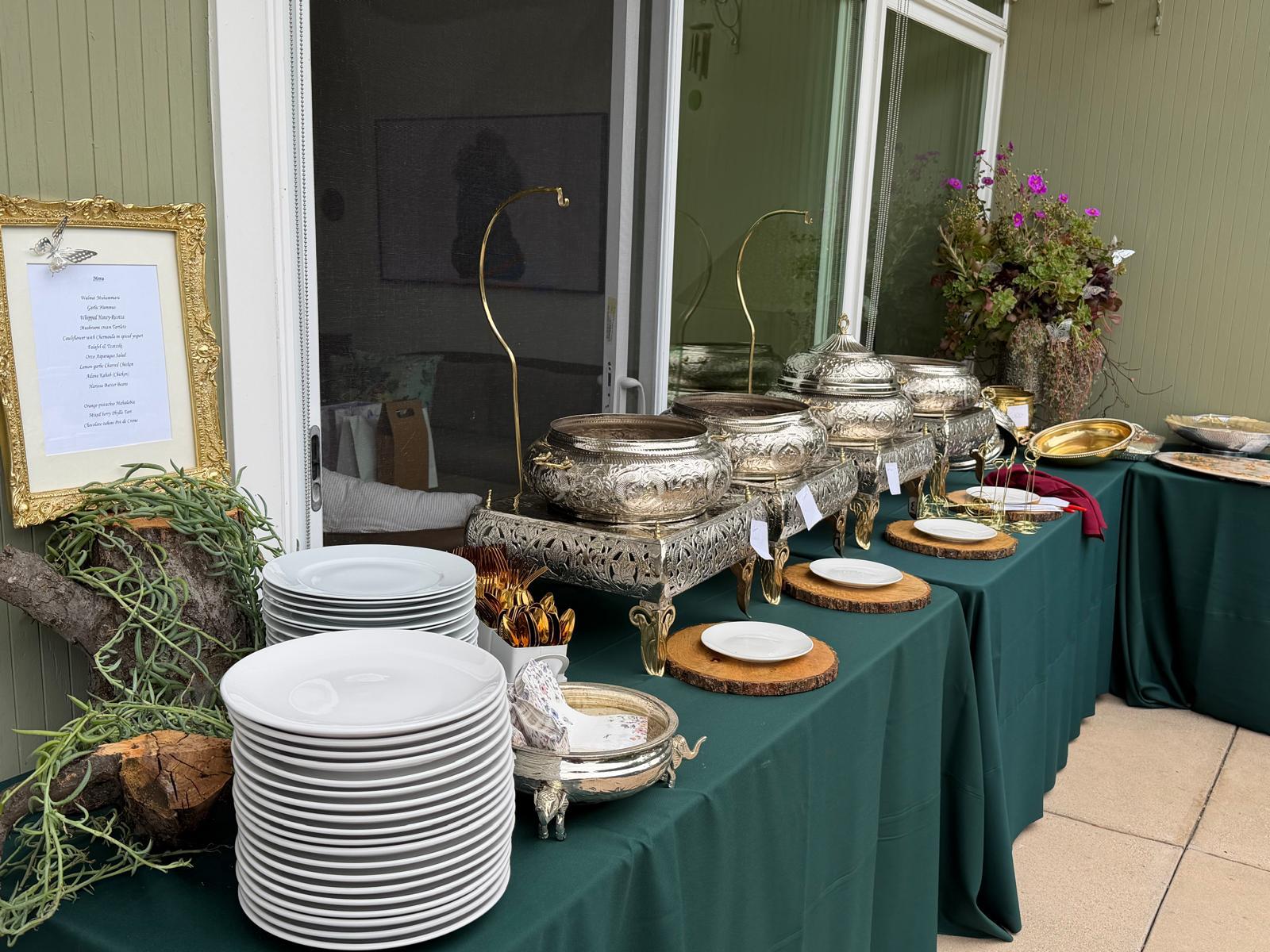 Outdoor buffet with plate stacks, gold cutlery, and a hand-written menu